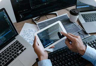 Hands Holding a Tablet in front of Various Computer Screens